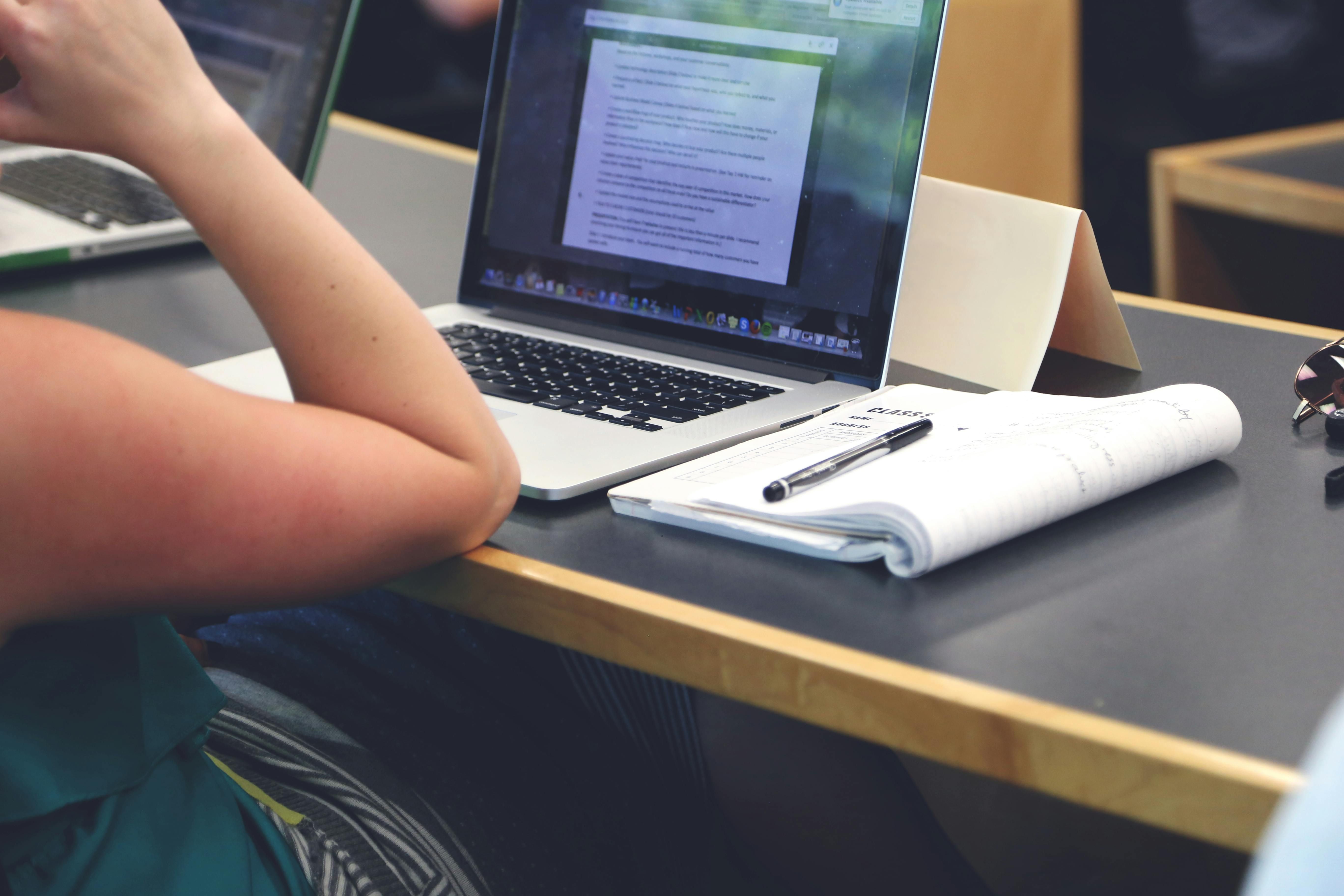 Schülerin arbeitet am Laptop mit Notizbuch und Stift