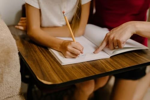 Lehrerin zeigt einer Schülerin beim Schreiben in einem Heft